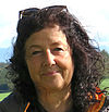 Porträtfoto einer Frau mit schwarzen Locken und einer Sonnenbrille in den Haaren. Sie steht in der Natur, das Sonnenlicht fällt von der rechten Seite auf ihr Gesicht.