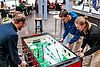 Drei Personen an Kicker-Tisch, spielen.