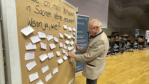 Kanzler Blomeyer heftet Post-It an Schautafel
