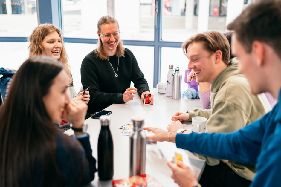 Eine Gruppe Studierender spielt Karten an einem Tisch in einer Cafeteria an der Universität Regensburg