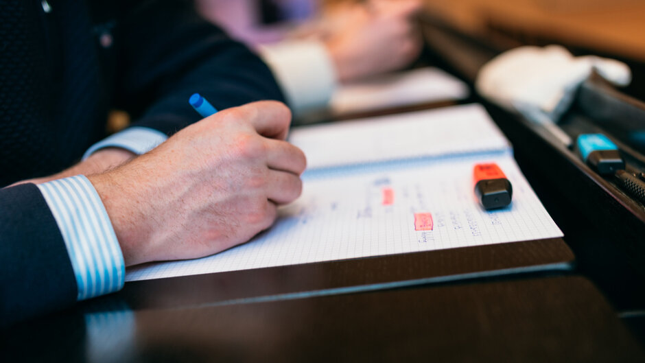 Eine Hand macht einen Hefteintrag. In den handschriftlichen Notizen sind zwei Stellen mit orangem Textmarker hervorgehoben.