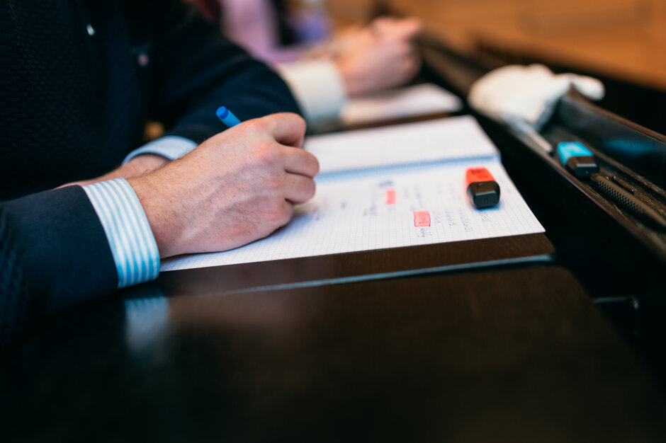 Eine Hand macht einen Hefteintrag. In den handschriftlichen Notizen sind zwei Stellen mit orangem Textmarker hervorgehoben.