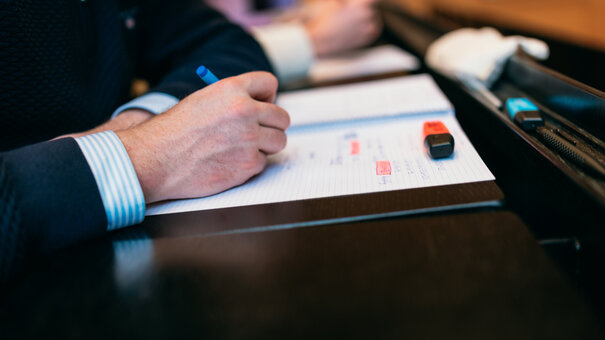 Eine Hand macht einen Hefteintrag. In den handschriftlichen Notizen sind zwei Stellen mit orangem Textmarker hervorgehoben.