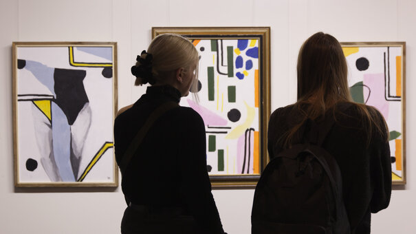 Zwei Frauen betrachten abstrakte Kunstwerke.