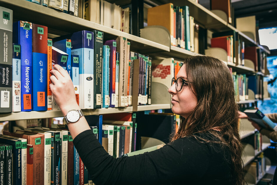 Eine junge Frau wählt an einem Bücherregal im Lesesaal Biologie der Universität Regensburg ein Buch aus.