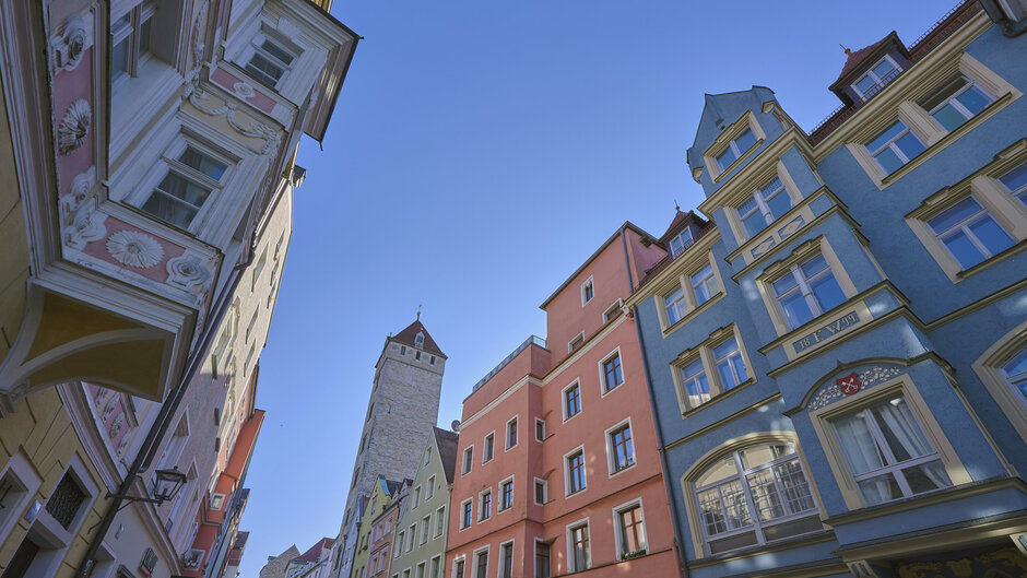 Bunte historische Häuserfassaden in der Regensburger Altstadt vor blauem Himmel aus der Froschperspektive fotografiert.