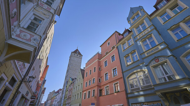 Bunte historische Häuserfassaden in der Regensburger Altstadt vor blauem Himmel aus der Froschperspektive fotografiert.