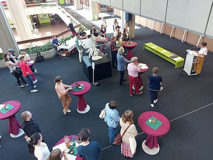 Die Ausstellungseröffnung mit Publikum an Stehtischen aus der Vogelperspektive. (öffnet Vergrößerung des Bildes)