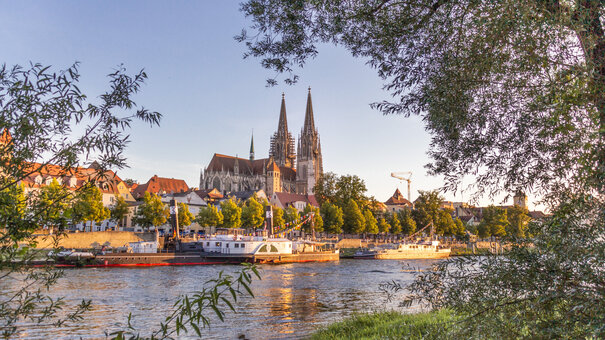 Blick auf die Donau, das südliche Ufer, Ausflugsschiffe und die Regensburger Altstadt. Im Hintergrund die Domspitzen.