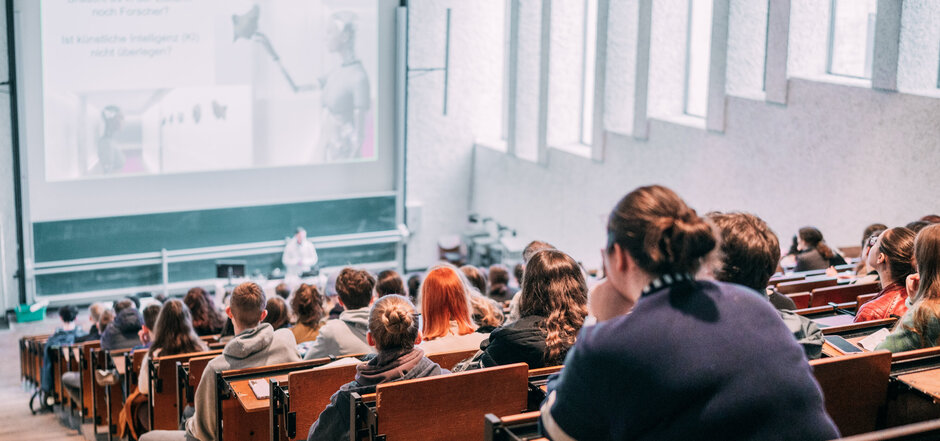Vorlesung in einem gut besuchten Hörsaal mit Tageslicht im Gebäudeteil Recht und Wirtschaft