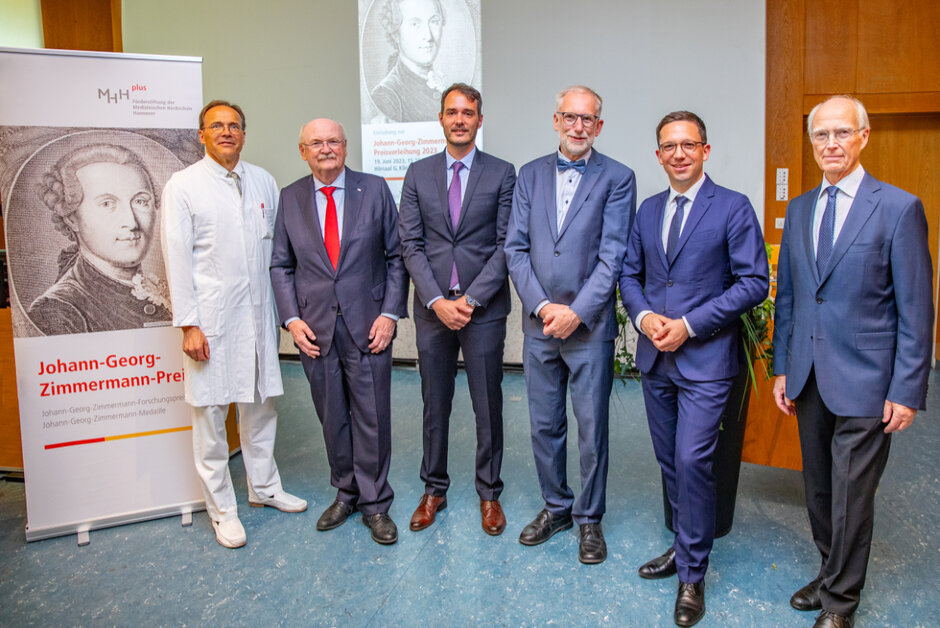 Gruppenfoto mit sechs Männern. Fünf davon tragen einen blauen Anzug, der sechste trägt weiße Kleidung inkl. Arztkittel. (öffnet Vergrößerung des Bildes)