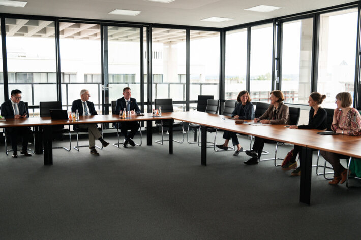 Mehrere Personen sitzen über Eck in einem Konferenzraum und unterhalten sich. (öffnet Vergrößerung des Bildes)