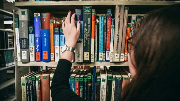 Eine Frau greift nach einem Buch in einem Bücherregal