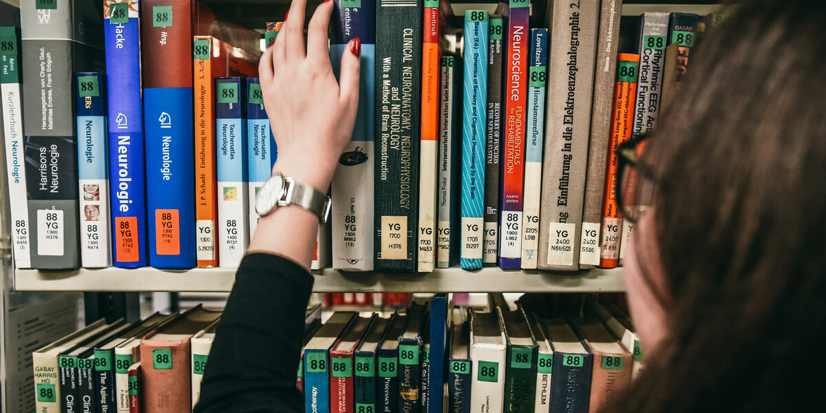 Eine Frau greift nach einem Buch in einem Bücherregal