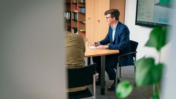 Ein Professor sitzt an einem Besprechungstisch und diskutiert mit seinen Mitarbeitern.