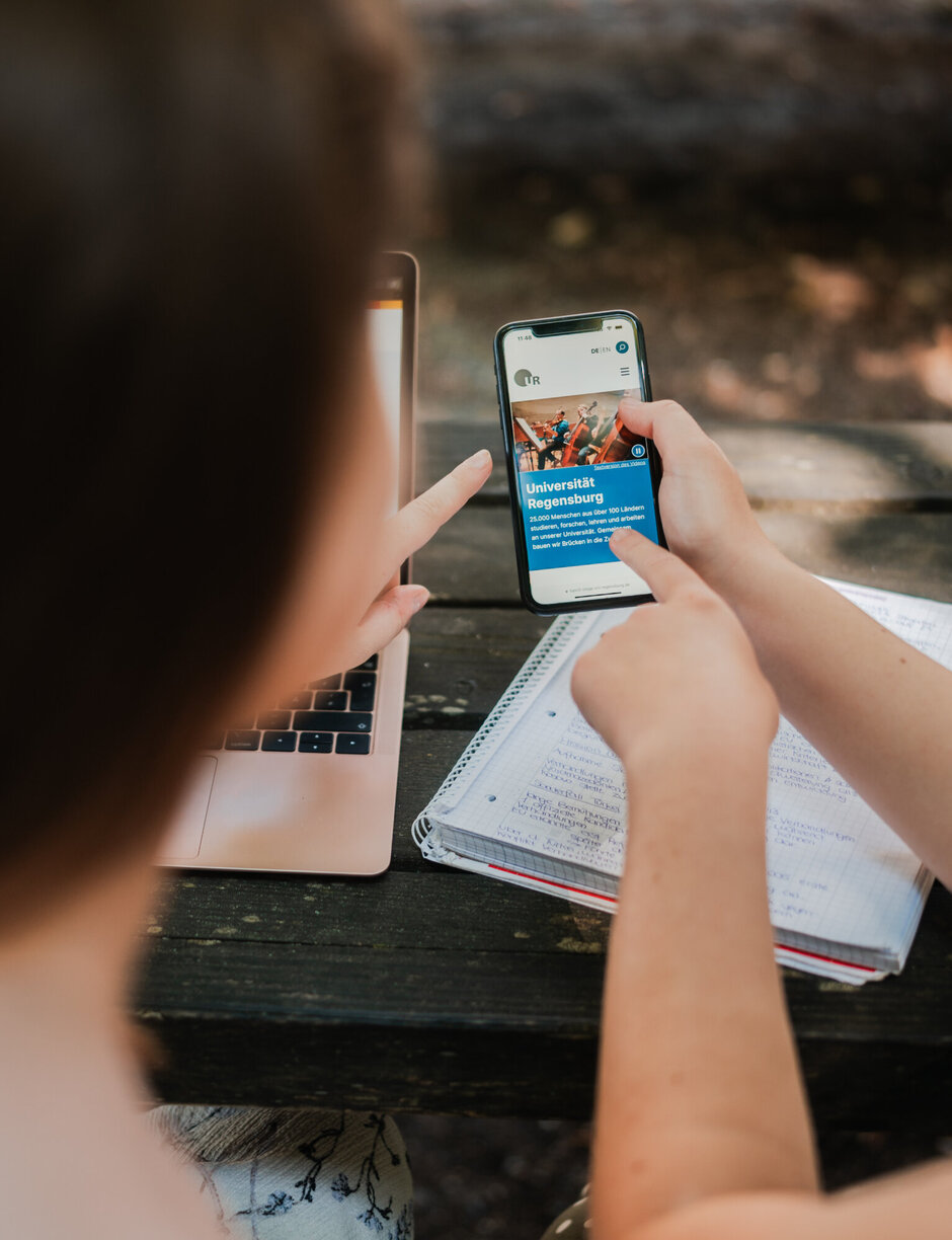 Zwei Personen betrachten ein Smartphone, das die neue Webseite der Universität Regensburg zeigt.