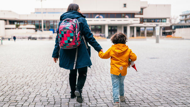 Eine erwachsene Person hält ein Kind an der Hand und geht mit ihm über das Forum der Universität Regensburg