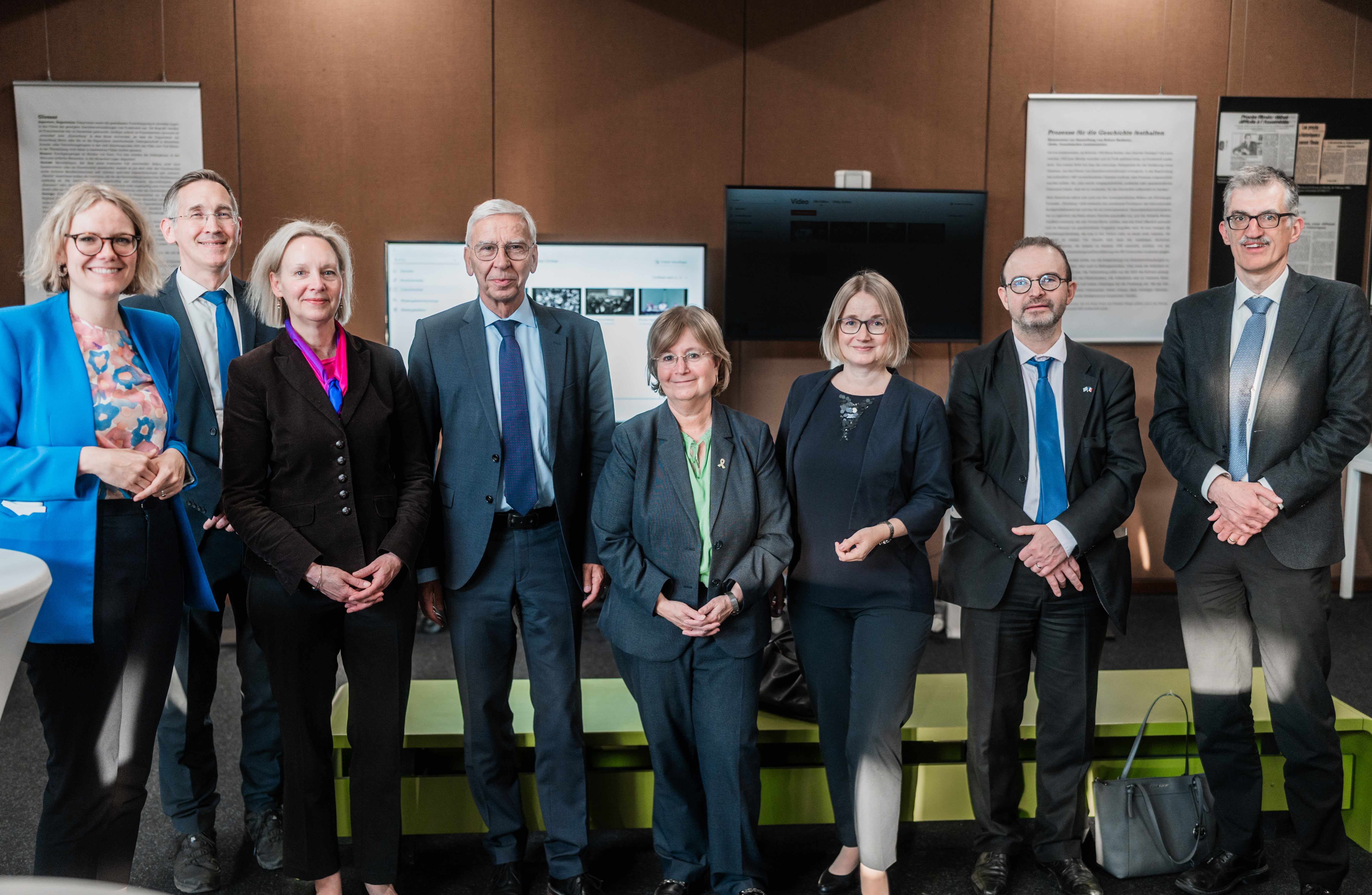 Eine Gruppe von Menschen steht nebeneinander und schaut in die Kamera. Im Hintergrund sind Stücke einer Ausstellung zu sehen. (öffnet Vergrößerung des Bildes)