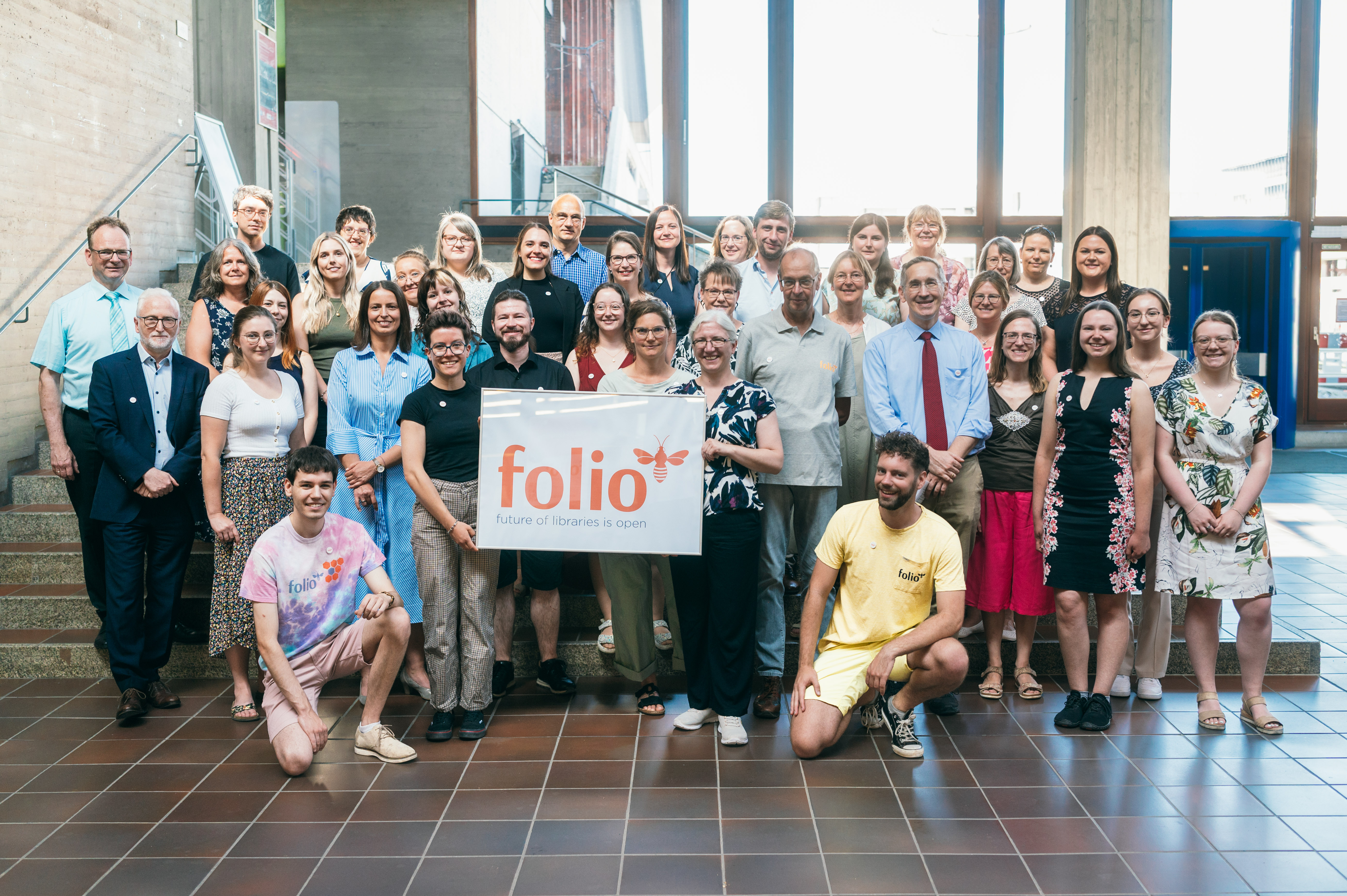 Gruppenbild mit vielen Personen, zwei halten ein Plakat auf dem "folio" steht. (öffnet Vergrößerung des Bildes)